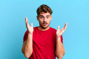 young adult caucasian man looking shocked and astonished, with jaw dropped in surprise when realizing something unbelievable