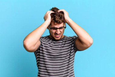 young adult caucasian man feeling stressed and frustrated, raising hands to head, feeling tired, unhappy and with migraine