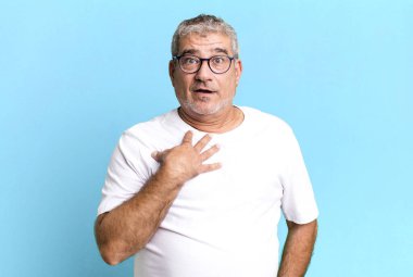 Orta yaşlı bir adam şok olmuş, şaşırmış ve şaşırmış hissediyor, elleri göğsünde ve ağzı açık, kim olduğunu söylüyor, ben mi??