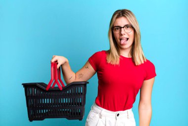 young pretty woman with cheerful and rebellious attitude, joking and sticking tongue out. empty shopping basket concept