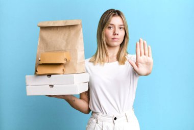 Genç ve güzel bir kadın ciddi görünüyor. Avuç içini gösteriyor. Durdurma hareketi yapıyor. Yemek teslimatı ve paket servis.