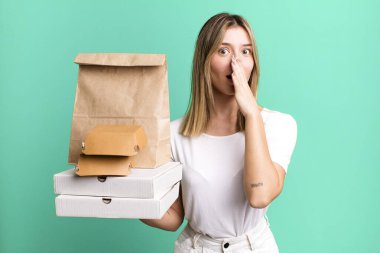 Genç ve güzel bir kadın şok olmuş bir şekilde elleriyle ağzını kapatıyor. Yemek teslimatı ve paket servis.