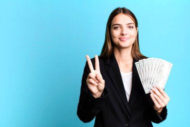 Genç, güzel bir bayan gülümsüyor ve iki numarayı gösteriyor. iş ve dolar banknotları kavramı