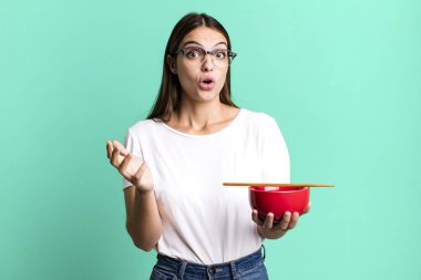 young pretty woman feeling extremely shocked and surprised. japanese ramen noodles concept