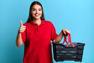 Genç ve güzel bir kadın gururlu, olumlu gülümsüyor. boş alışveriş sepeti kavramı