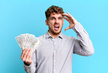 Genç, beyaz bir adam ellerini havaya kaldırarak çığlık atıyor. Dolar banknotları konsepti