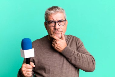 Orta yaşlı, ağzı ve gözleri açık ve elleri çenesinde olan bir adam. Mikro bilgisayarlı gazeteci ya da TV sunucusu