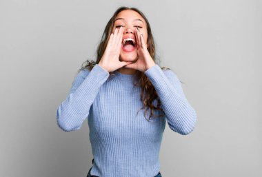 Genç, güzel bir kadın mutlu, heyecanlı ve pozitif hissediyor. Elleri ağızda, bağırıyor.