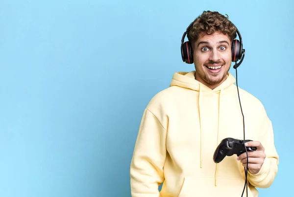 stock image young adult caucasian man looking happy and pleasantly surprised with headset and a controller. gamer concept