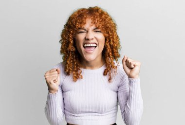 kızıl saçlı güzel bir kadın mutlu, şaşırmış ve gururlu, bağırıyor ve başarıyı büyük bir gülümsemeyle kutluyor.