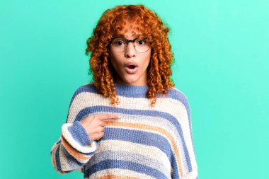 Kızıl saçlı güzel bir kadın şok olmuş ve şaşırmış görünüyor ağzı açık, kendini işaret ediyor.