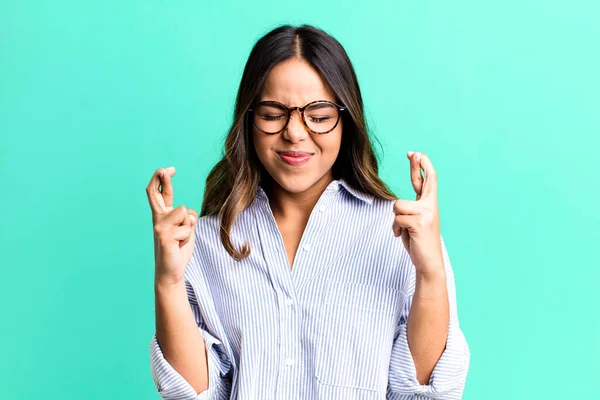 stock image hispanic pretty woman smiling and anxiously crossing both fingers, feeling worried and wishing or hoping for good luck