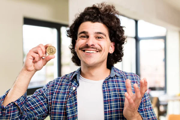自宅のインテリアでビットコインのコインを持つ若いハンサムな男 — ストック写真