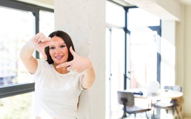 young adult pretty woman feeling happy, friendly and positive, smiling and making a portrait or photo frame with hands