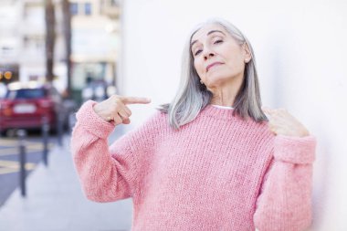 Yaşlı, emekli, güzel, beyaz saçlı, kötü tavırlı, gururlu ve agresif görünen, yukarıyı gösteren ya da elleriyle alay eden bir kadın.