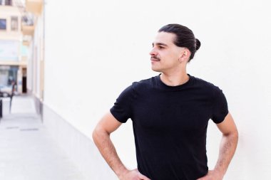 Genç havalı adam mutlu, neşeli ve kendinden emin görünüyor, gururla gülümsüyor ve iki elini de kalçasında istiyor.