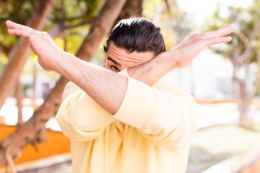 Genç, havalı bir adam yüzünü eliyle kapatıyor ve kamerayı durdurmak için diğer elini öne koyuyor. Fotoğraf ya da resimleri reddediyor.