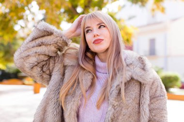 Genç, güzel bir kadın şaşkın ve kafası karışmış hissediyor, başını kaşıyor ve yan tarafa bakıyor.