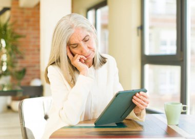 Yaşlı, güzel bir kadın, dokunmatik ekranlı yorucu bir olaydan sonra sıkılmış, hayal kırıklığına uğramış ve uykulu hissediyor.
