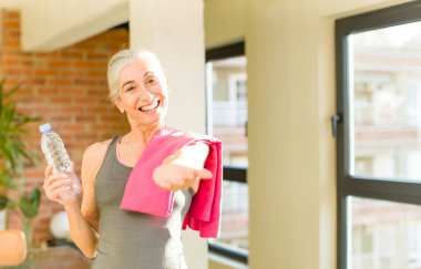 Kıdemli güzel bayan mutlu bir şekilde gülümsüyor ve bir konsept sunuyor veya gösteriyor. fitness konsepti