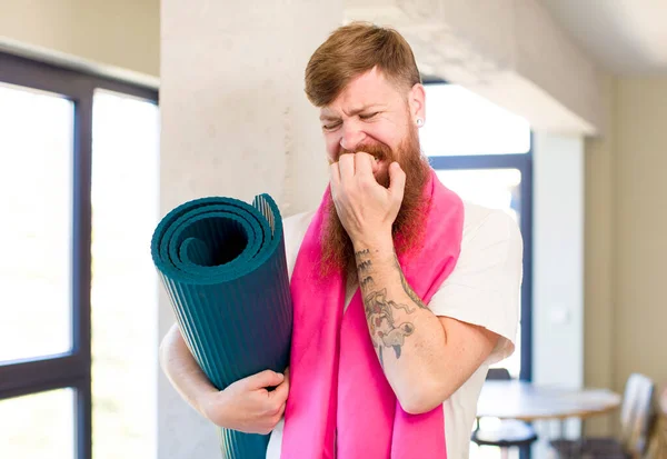 红头发的男人感到害怕 担心或生气 用瑜伽垫向旁边看 健身概念 — 图库照片