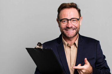 Orta yaşlı bir adam neşeli bir şekilde gülümsüyor, mutlu hissediyor ve envanterle bir tarafı işaret ediyor. iş kavramı