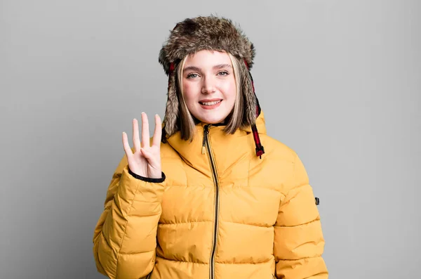 young pretty woman smiling and looking friendly, showing number four. cold and coat concept