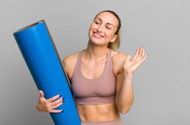 young pretty woman smiling happily, waving hand, welcoming and greeting you. fitness and yoga concept