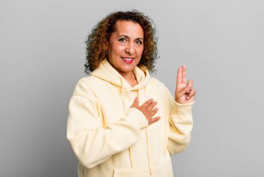 Orta yaşlı İspanyol kadın mutlu, kendinden emin ve güvenilir görünüyor, gülümsüyor ve zafer işareti gösteriyor, olumlu bir tavırla.