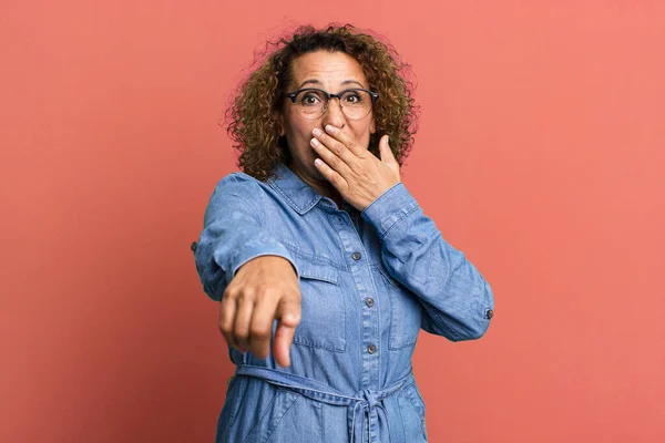 middle age hispanic woman laughing at you, pointing to camera and making fun of or mocking you