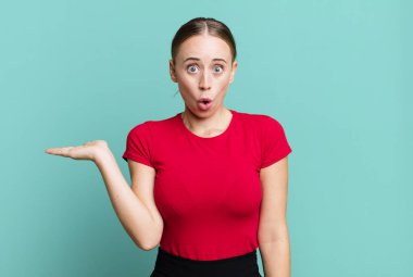 Şaşırmış ve şoke olmuş bir halde, çenesi düşmüş bir objeyi elinde açık bir elle tutarken.