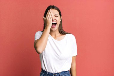 pretty young adult woman looking sleepy, bored and yawning, with a headache and one hand covering half the face