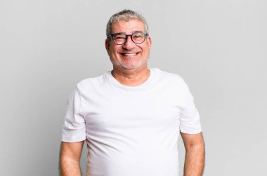 Orta yaşlı bir adam mutlu ve şapşal görünüyor. Geniş, eğlenceli, kaçık bir gülüşü ve açık gözleri var.