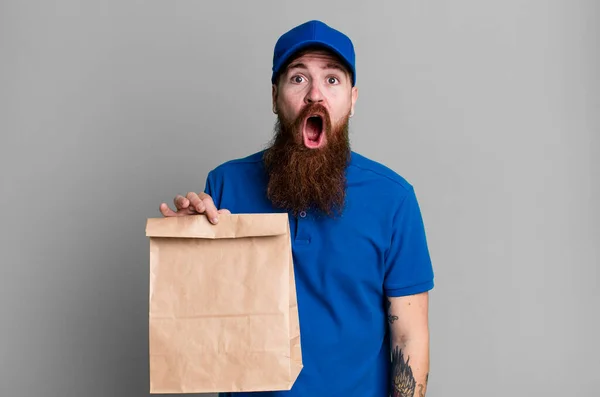 若い大人の赤い髪の髭のクールな配達人と紙袋 — ストック写真