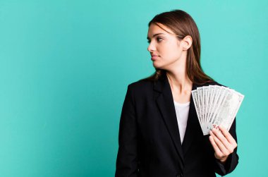 Profil görünümlü genç, güzel bir kadın hayal kuruyor ya da hayal kuruyor. iş ve dolar banknotları kavramı