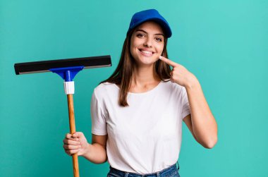 Genç ve güzel bir kadın, kendine güvenerek gülümsüyor. Pencere temizleme kavramı