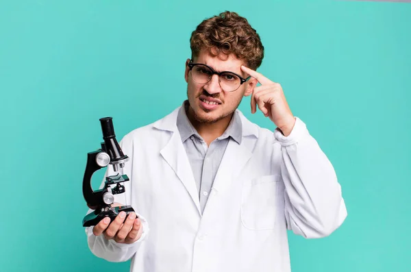若い大人の白人男性は混乱して困惑してるあなたが狂ってることを示す 顕微鏡の概念を持つ科学研究室の学生は — ストック写真