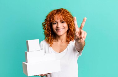 Kızıl saçlı güzel bayan gülümsüyor ve arkadaş canlısı görünüyor, iki numarayı gösteriyor. boş paket kutusu kavramı