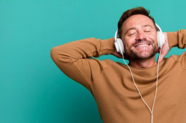 Orta yaşlı bir adam kulaklıklarıyla müzik dinliyor futbol topu ile spor koçluğu yapıyor.