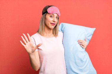Güzel sarışın kadın gülümsüyor ve arkadaş canlısı görünüyor, beş numarayı gösteriyor. Pijama ve gecelik konsepti