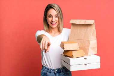 Güzel sarışın kadın seni seçen kamerayı işaret ediyor. Kağıt fast food paketleri götürür.