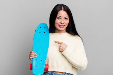 hispanic pretty woman smiling cheerfully, feeling happy and pointing to the side. skate boarding concept