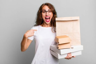 İspanyol güzel kadın kendini mutlu hissediyor ve heyecanla kendini işaret ediyor. Fast food paketleri kavramını kaldır