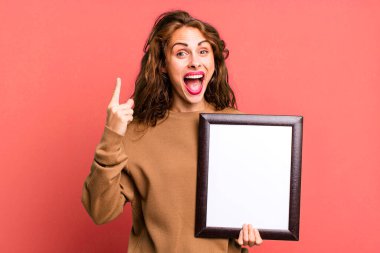 hispanic pretty woman feeling like a happy and excited genius after realizing an idea with an empty blank frame