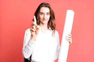 young pretty woman smiling proudly and confidently making number one. architect concept