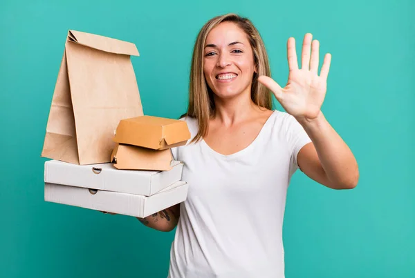 かなりブロンドの女性は笑顔で友好的に見える5番目を示してる 配送は食品パッケージの概念を取り除き — ストック写真