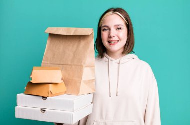 Genç ve güzel bir kadın mutlu bir şekilde gülümsüyor, eli kalçasında ve kendinden emin. Fast food konseptini kaldır.
