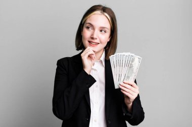 Genç ve güzel bir kadın, mutlu ve kendinden emin bir ifadeyle gülümsüyor, elleri çenesinde. Dolar banknotları