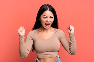pretty latin woman feeling happy, positive and successful, celebrating victory, achievements or good luck