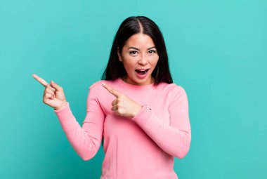 Güzel Latin bir kadın kendini neşeli ve şaşırmış hissediyor. Şok olmuş bir ifadeyle gülümsüyor ve bir tarafı işaret ediyor.